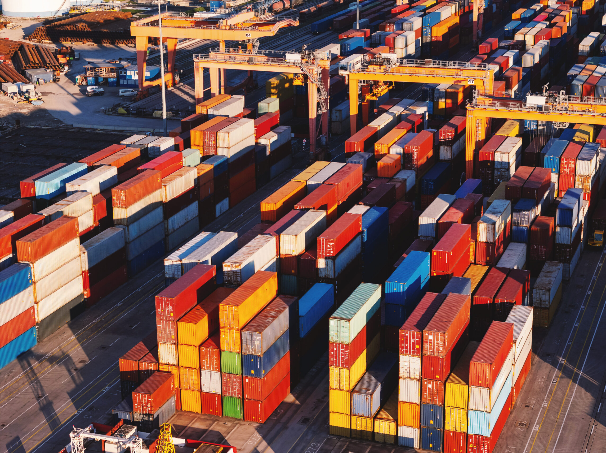 Cargo containers stacked at a commercial shipping port with cranes working